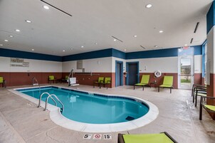 Una piscina con una profundidad máxima de 1.5 metros y un letrero que indica una profundidad máxima de 4.5 metros, rodeada de sillas verdes y un suelo de baldosas.