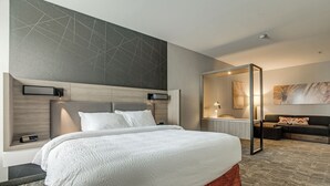Ein modernes Hotelzimmer mit einem großen Bett, einem integrierten Schreibtisch, einer Sitzecke und einem großen Spiegel.