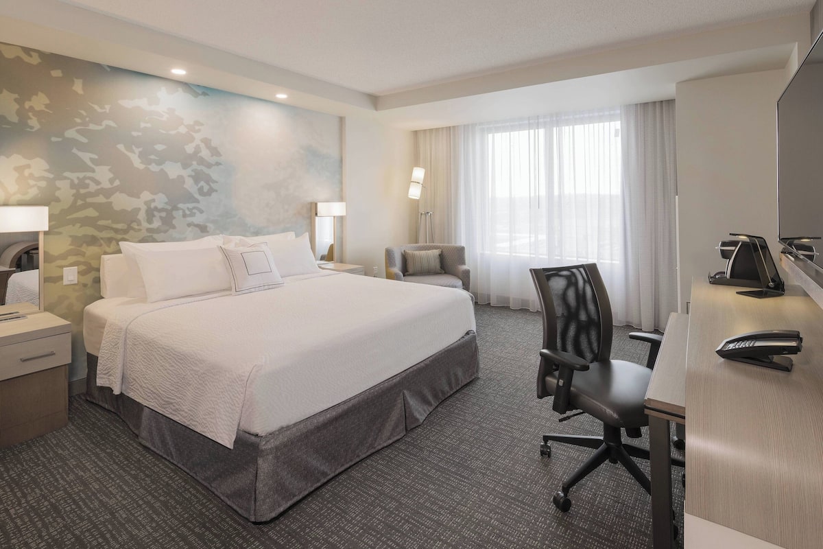 A hotel room with a large bed, a desk with a telephone, a chair, and a lamp.
