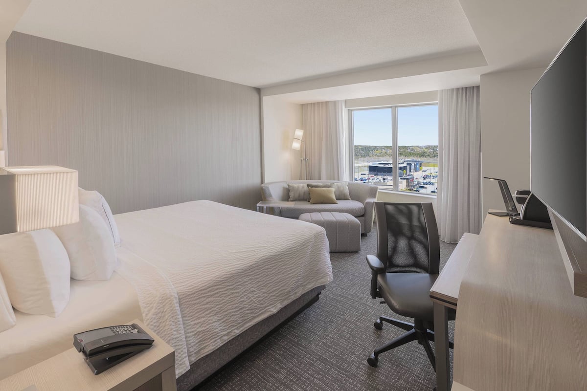 A hotel room with a large bed, a desk, a chair, a sofa, and a TV.
