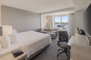 A hotel room with a large bed, a desk, a chair, a sofa, and a TV.