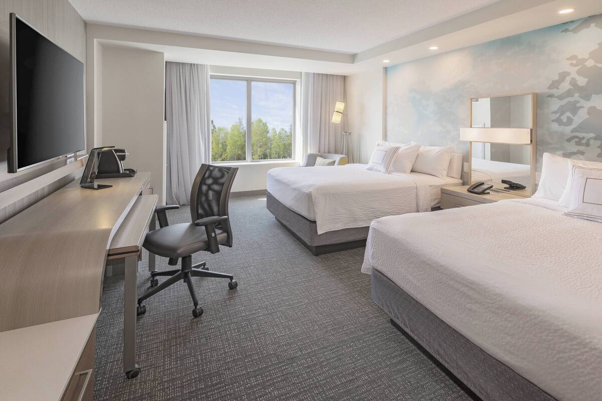 A hotel room with a bed, a desk with a chair, a TV, and a window with curtains.