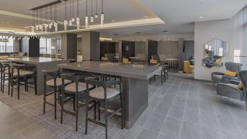 Un vestíbul d'hotel modern amb una zona de bar central, zones d'estar i un gran mirall a la paret.
