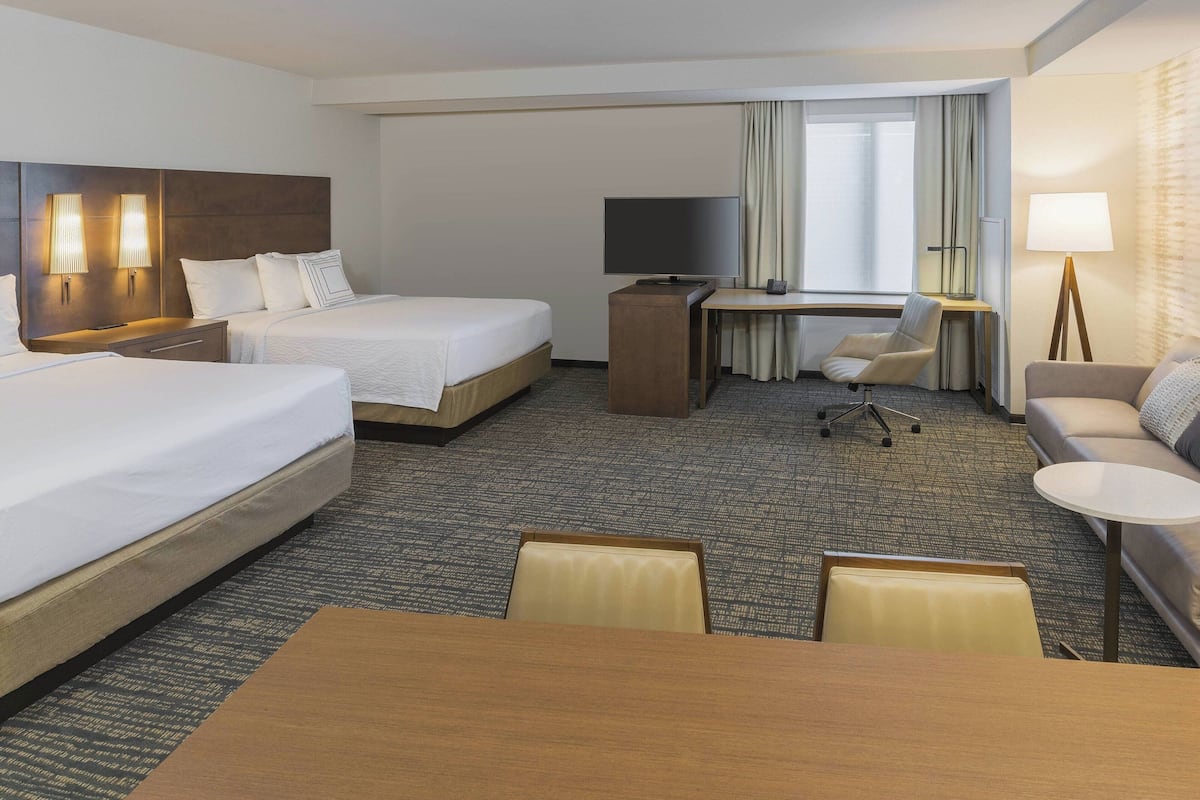 A hotel room with two beds, a desk, a TV, a chair, a sofa, and a table.