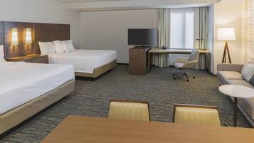Habitación de hotel con dos camas, un escritorio, televisor, silla, sofá y mesa.