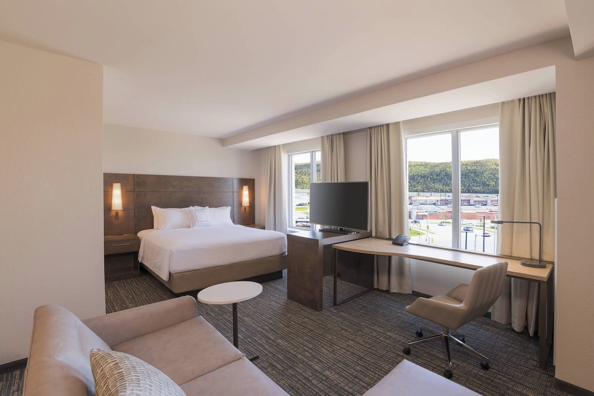 A hotel room with a bed, a desk with a TV, a chair, and a sofa.