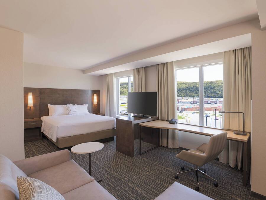 Una habitación de hotel con cama, escritorio con televisor, silla y sofá.