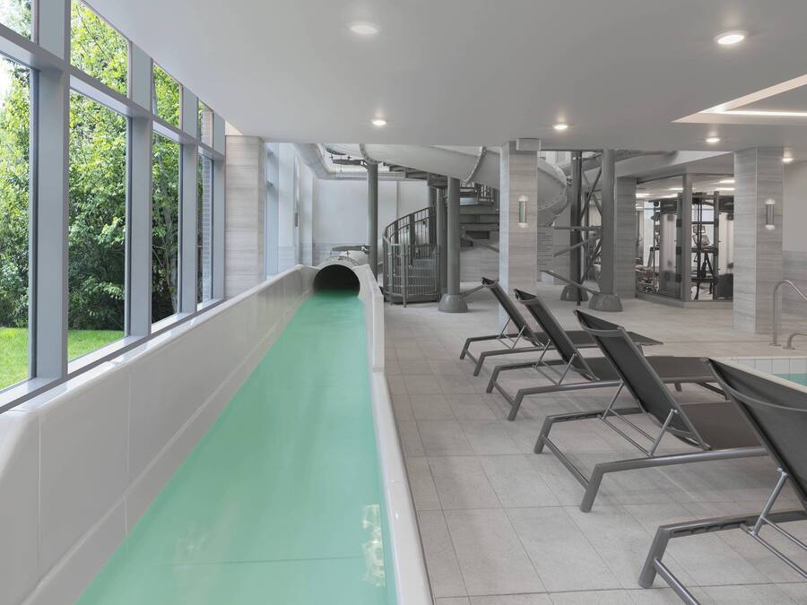 Piscina interior moderna com uma faixa verde, grandes janelas e uma escadaria que dá acesso a uma área de ginásio.