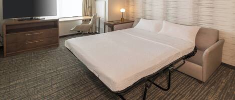 A hotel room with a bed, a TV, a desk, and a chair.