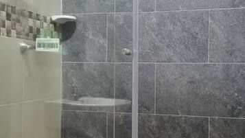Un área de ducha con puerta de vidrio, paredes con azulejos y un dispensador de jabón.
