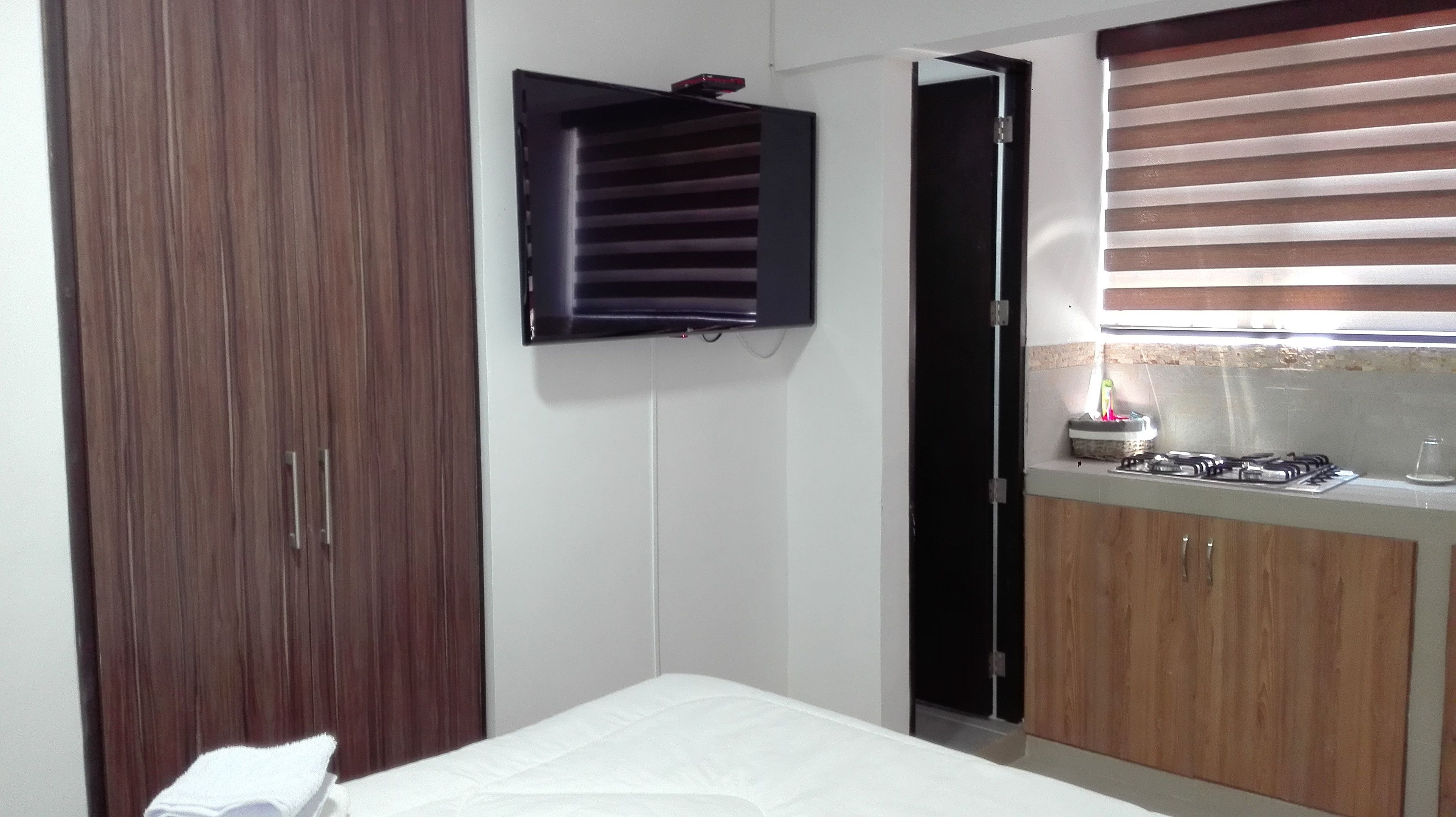 Un dormitorio con un armario de madera, una mesita de noche pequeña y una ventana con persianas.