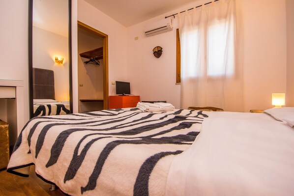 Habitación de hotel con colcha a rayas de cebra, televisor de pantalla plana, cabecero de madera y aire acondicionado instalado en la pared.