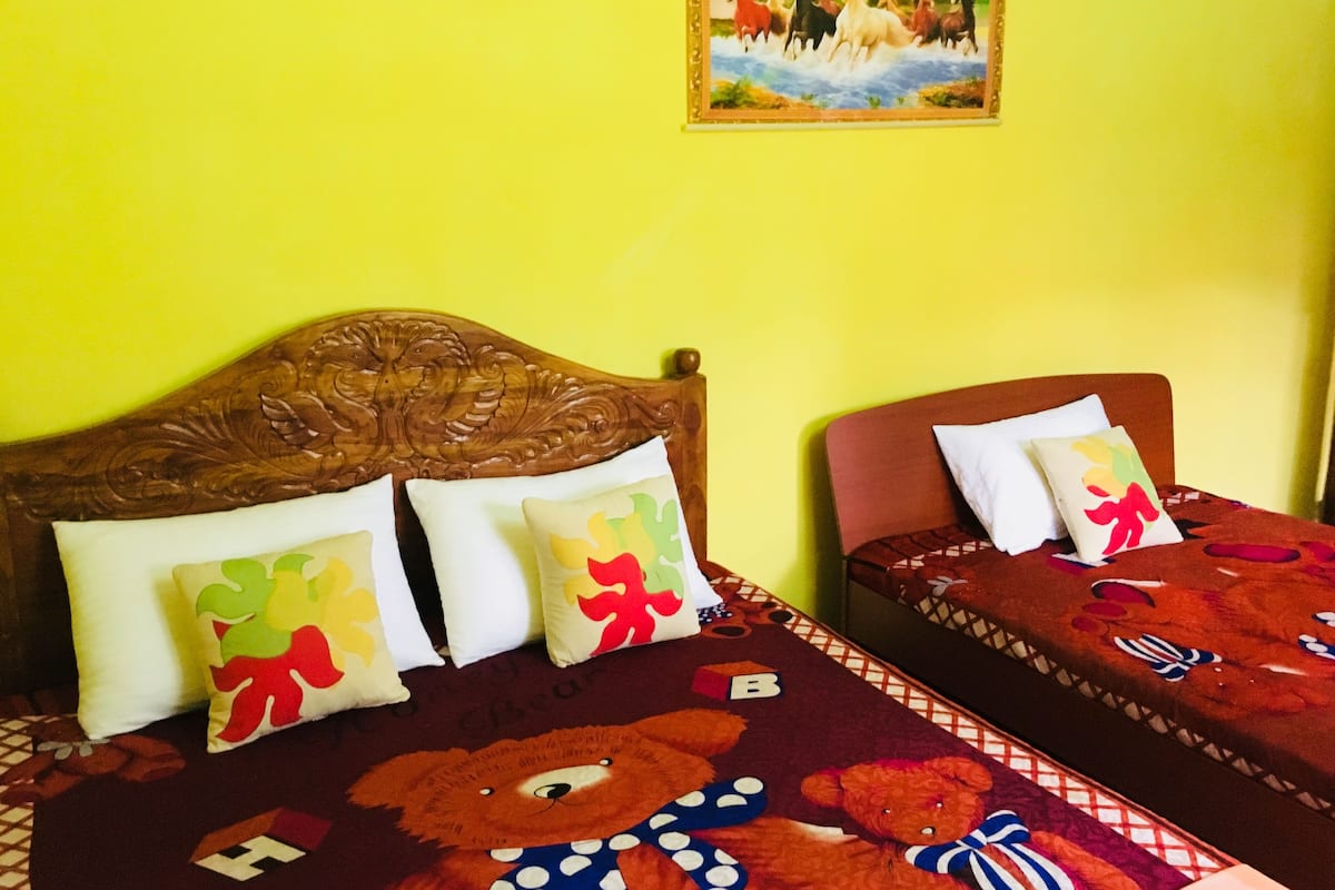 A room with two beds, each with a wooden headboard and a colorful bedspread featuring a teddy bear design. There is a painting on the wall above the beds.