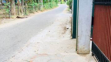 A paved pathway leading to a gated entrance with a metal fence and a concrete pillar.