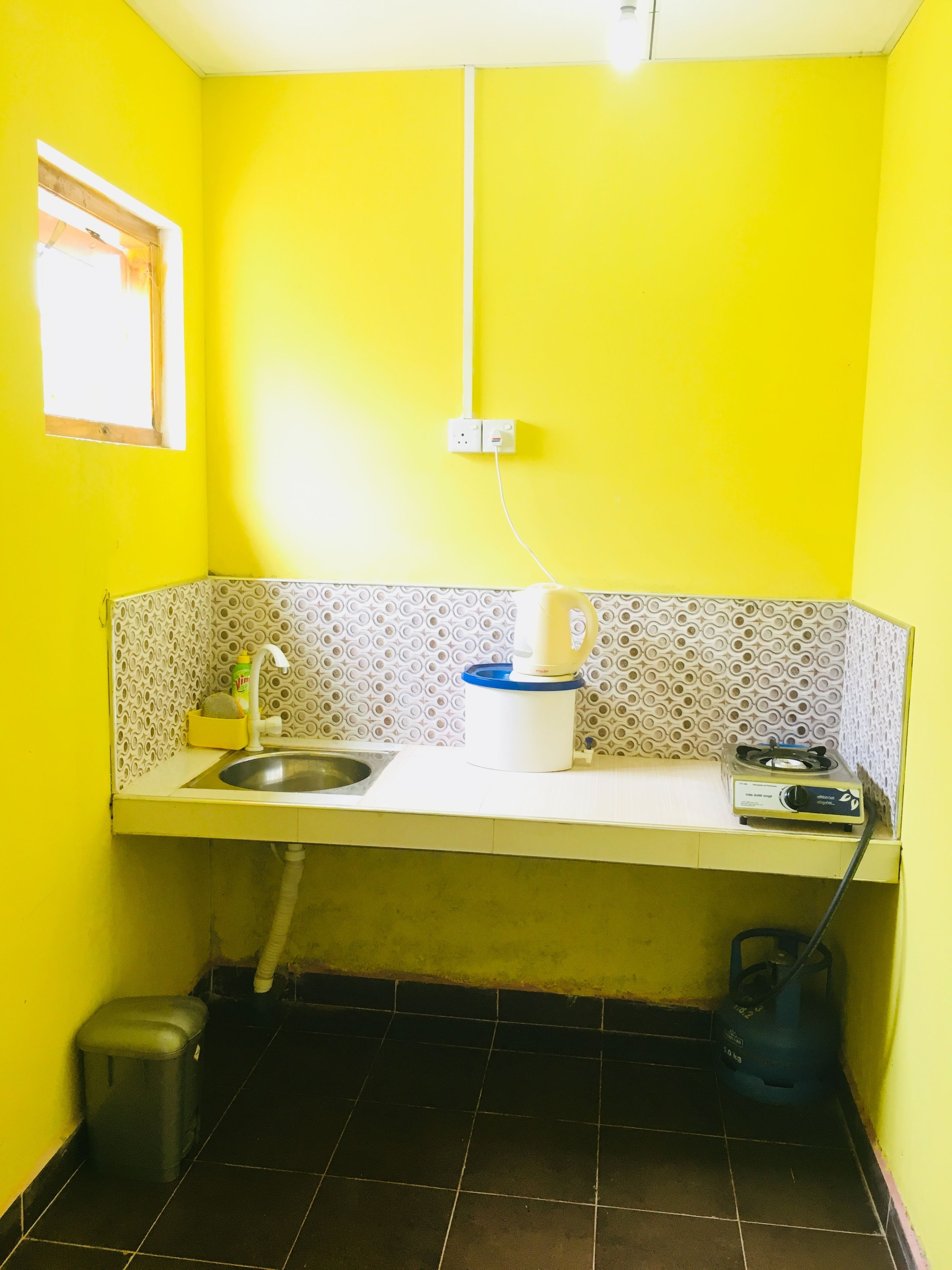Uma cozinha compacta com pia, chaleira, fogão a gás e lixeira.