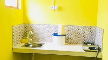 Uma cozinha compacta com pia, chaleira, fogão a gás e lixeira.