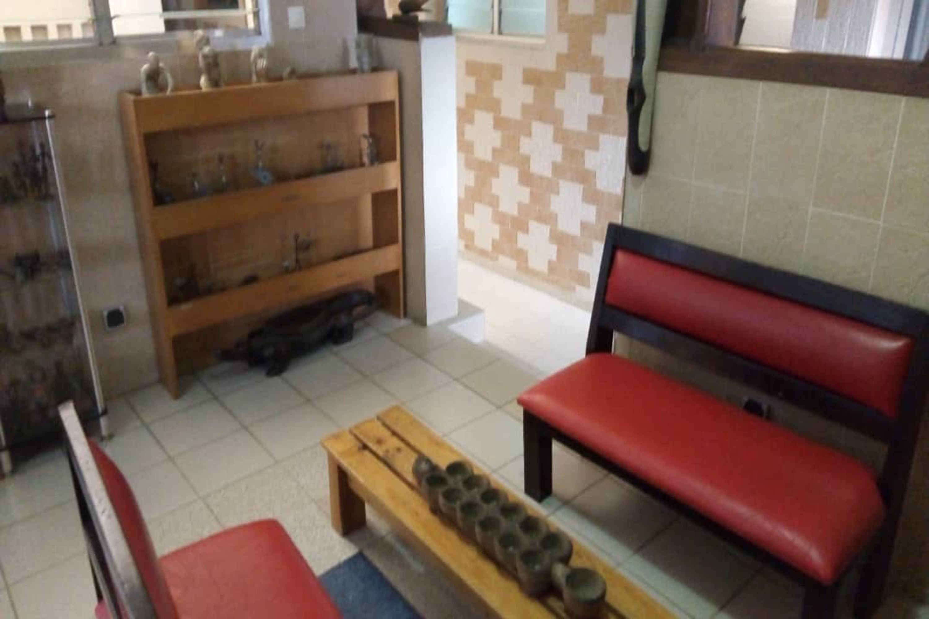 A kitchen with a wooden bench, a shelf with kitchen utensils, and a tiled backsplash.