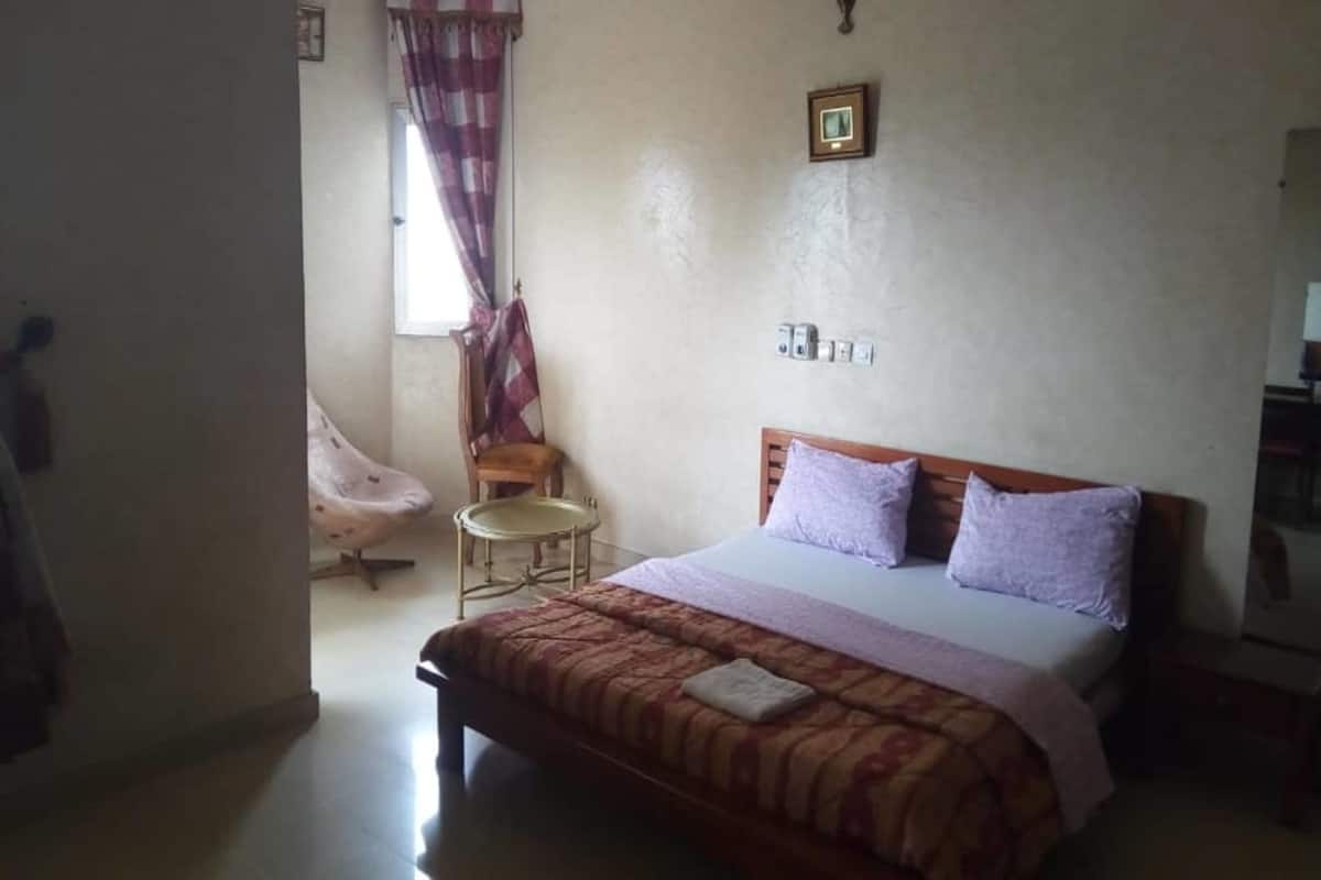 A bedroom with a bed, a chair, a small table, and a window with curtains.