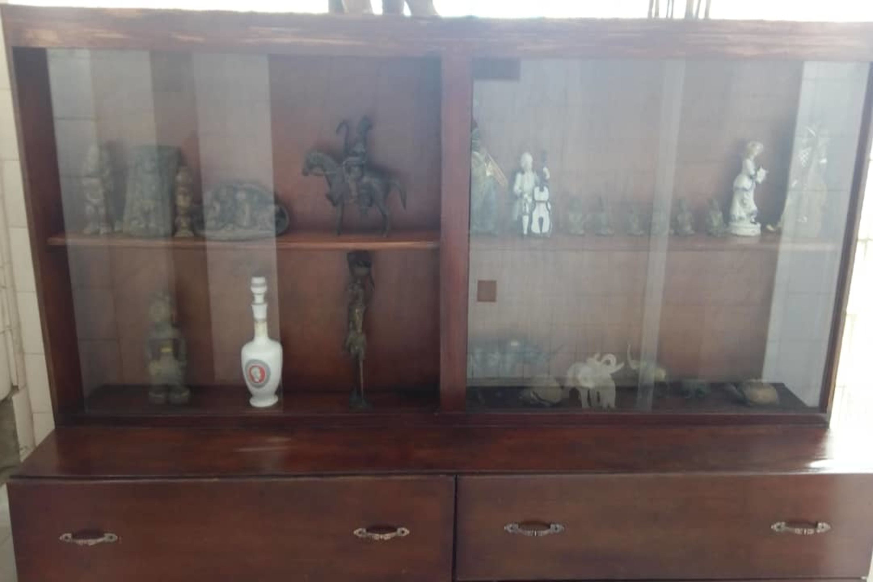A wooden display cabinet with glass doors, containing various figurines and a bottle.