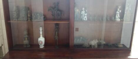 A wooden display cabinet with glass doors, containing various figurines and a bottle.