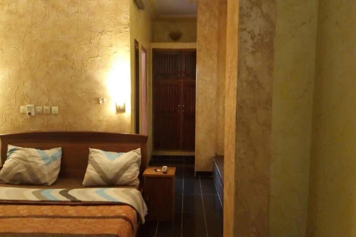 A hotel room with a bed, bedside table, and a door leading to a bathroom.