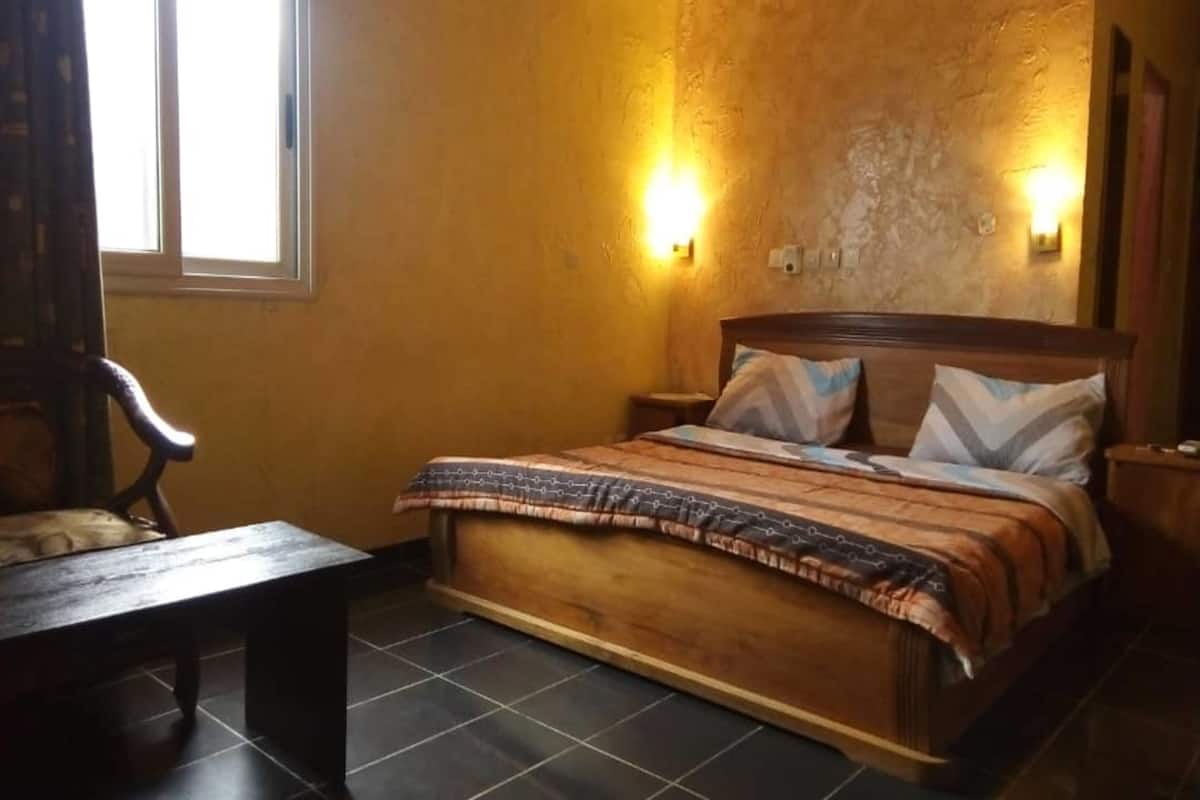 A bedroom with a wooden bed, two bedside lamps, a bench, and a window.