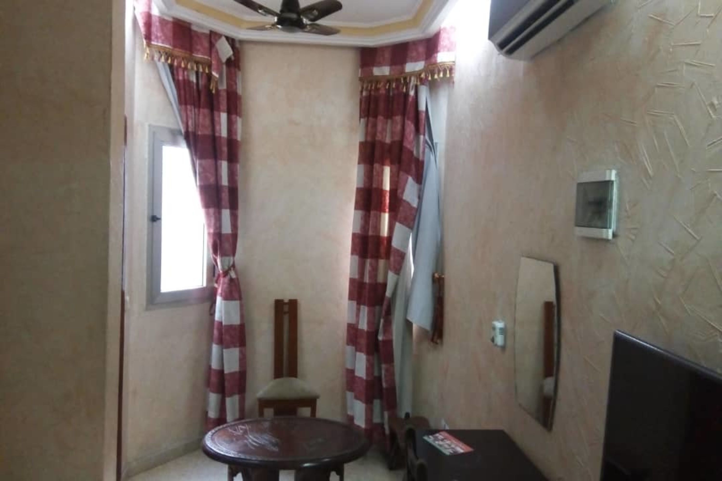 Una habitación con ventilador de techo, una mesa redonda, dos sillas, un televisor y un aire acondicionado de pared.