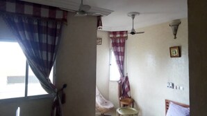 A room with a ceiling fan, a window with checkered curtains, a chair, and a bed.