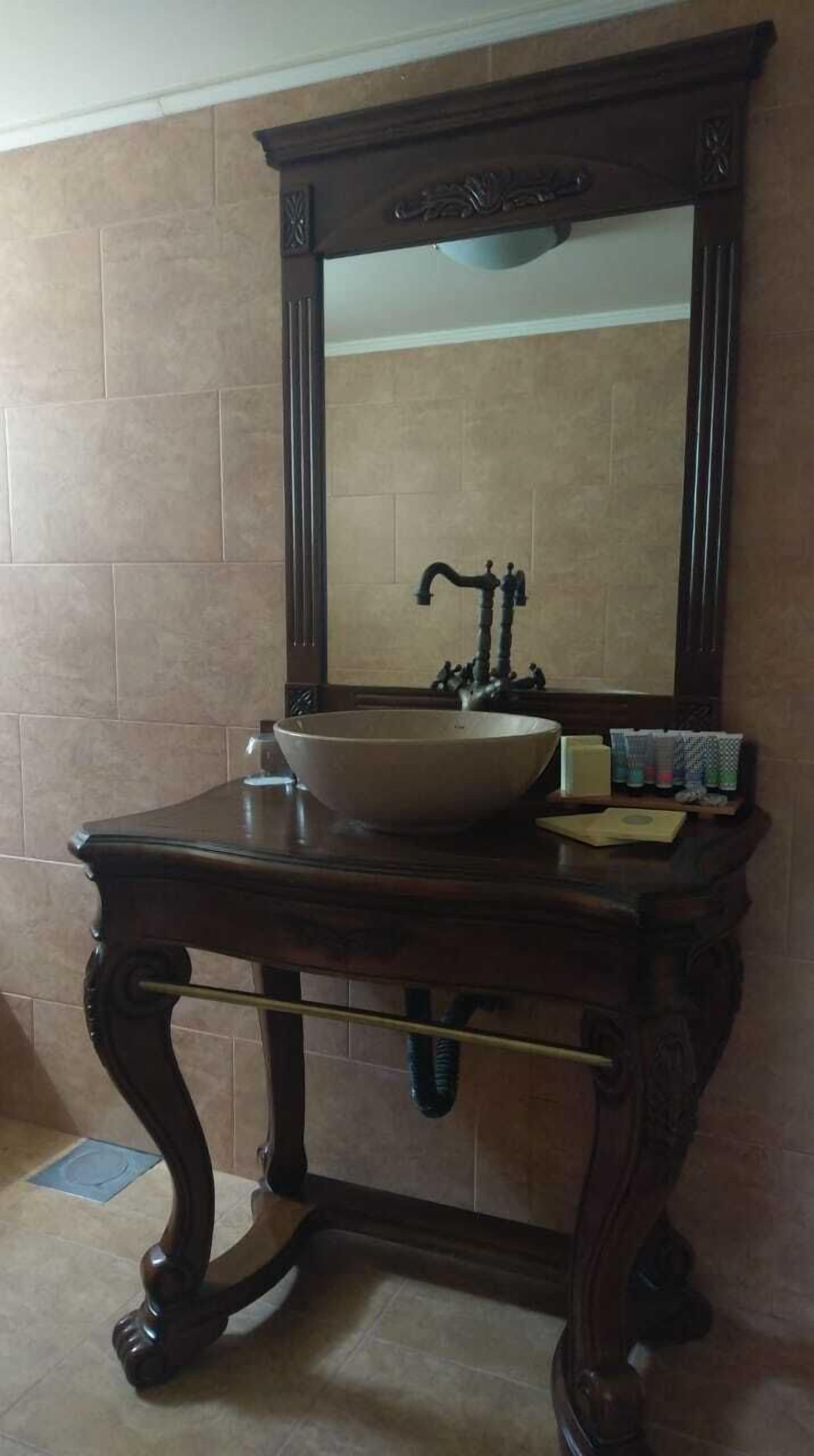 Un baño con tocador de madera, un espejo grande, un lavamanos y un perchero para toallas.