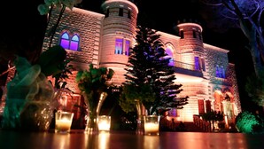 Un bâtiment qui ressemble à un château, avec des fenêtres en arc et une tourelle, illuminé la nuit.