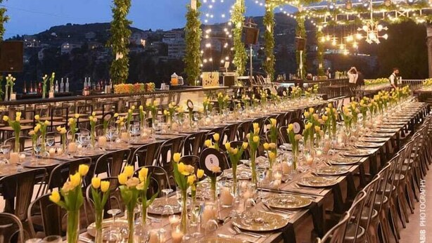 Un espace de restauration en plein air agrémenté de guirlandes lumineuses et de plantes suspendues, avec des tables dressées, des assiettes, des verres et des bougies.