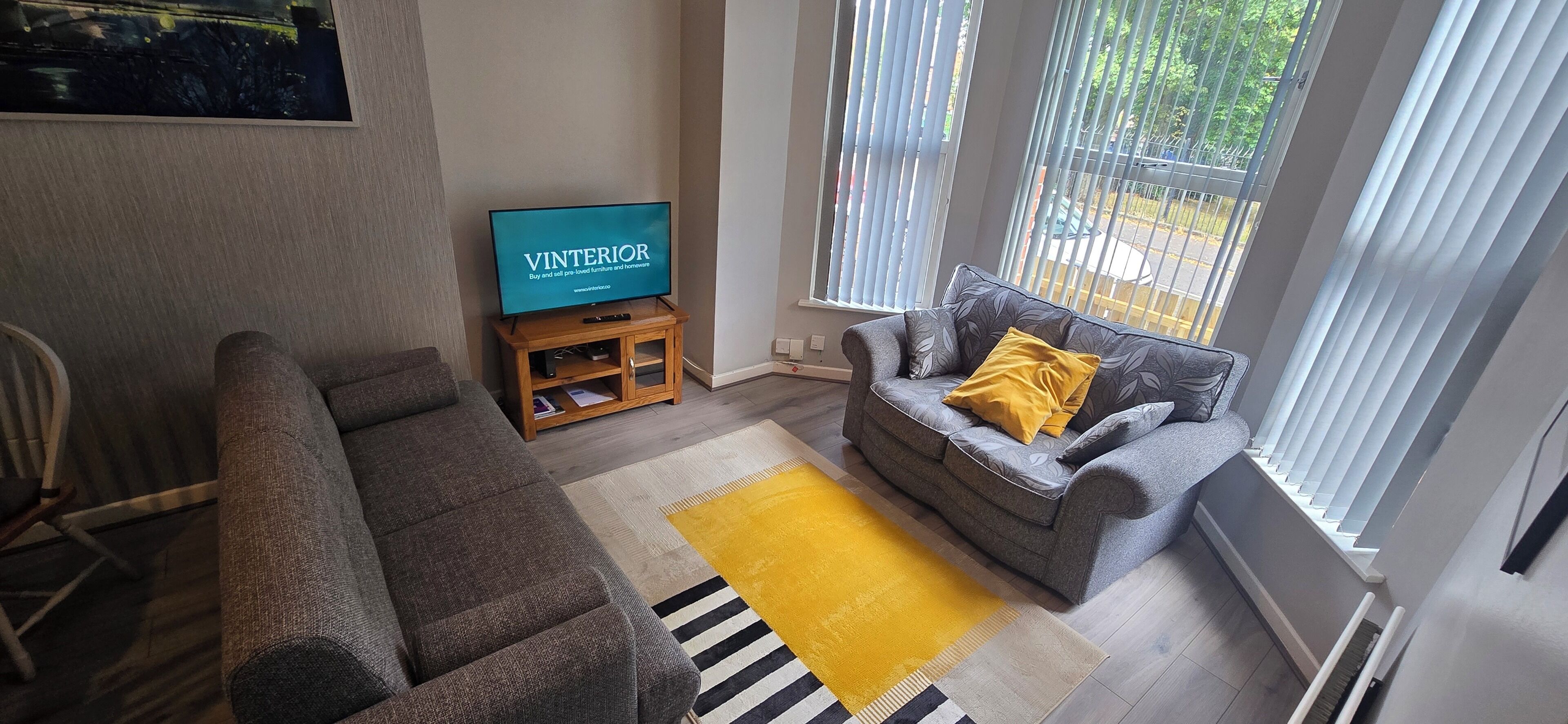 A living room with a grey sofa, a yellow rug, and a TV on a wooden stand.