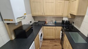 A compact kitchen with wooden cabinets, a washing machine, a sink, and a stove. - Castleton Gardens Apartments Belfast (Belfast)