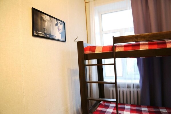 Una cama litera con colcha de cuadros, un cuadro enmarcado en la pared y una ventana con cortinas.
