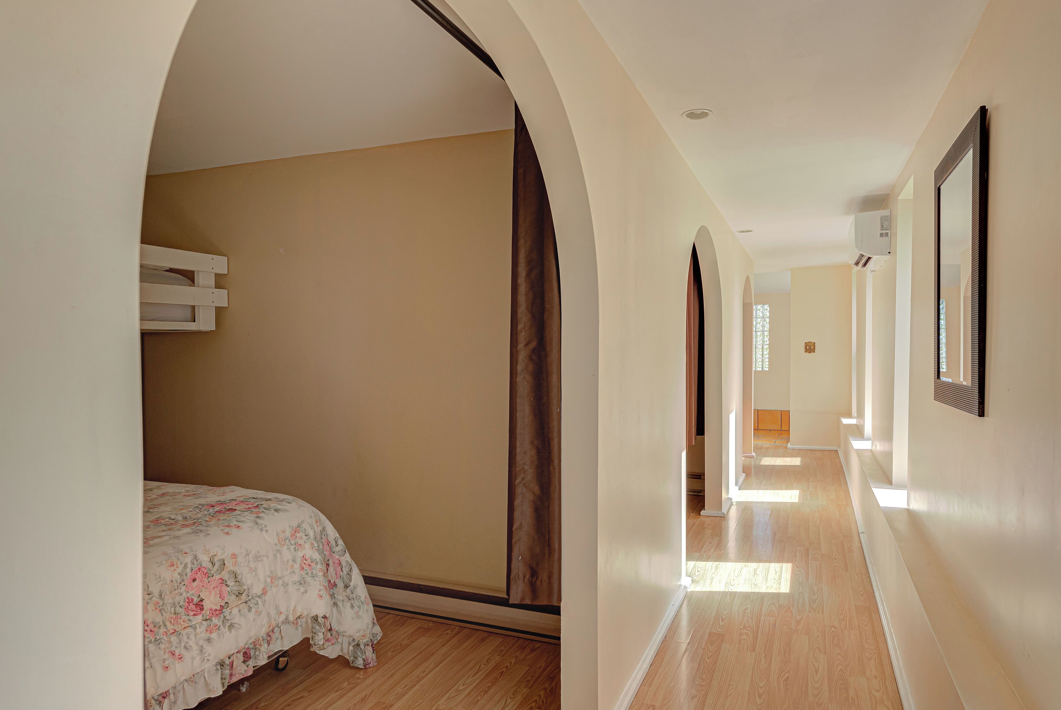 A hallway with a bed, wooden flooring, and a large mirror on the wall.