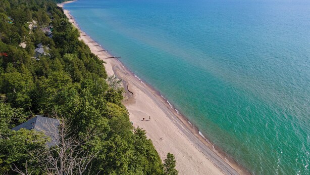 Vue aérienne d’une plage aux eaux turquoise et limpides, bordée d’une forêt verdoyante et luxuriante.