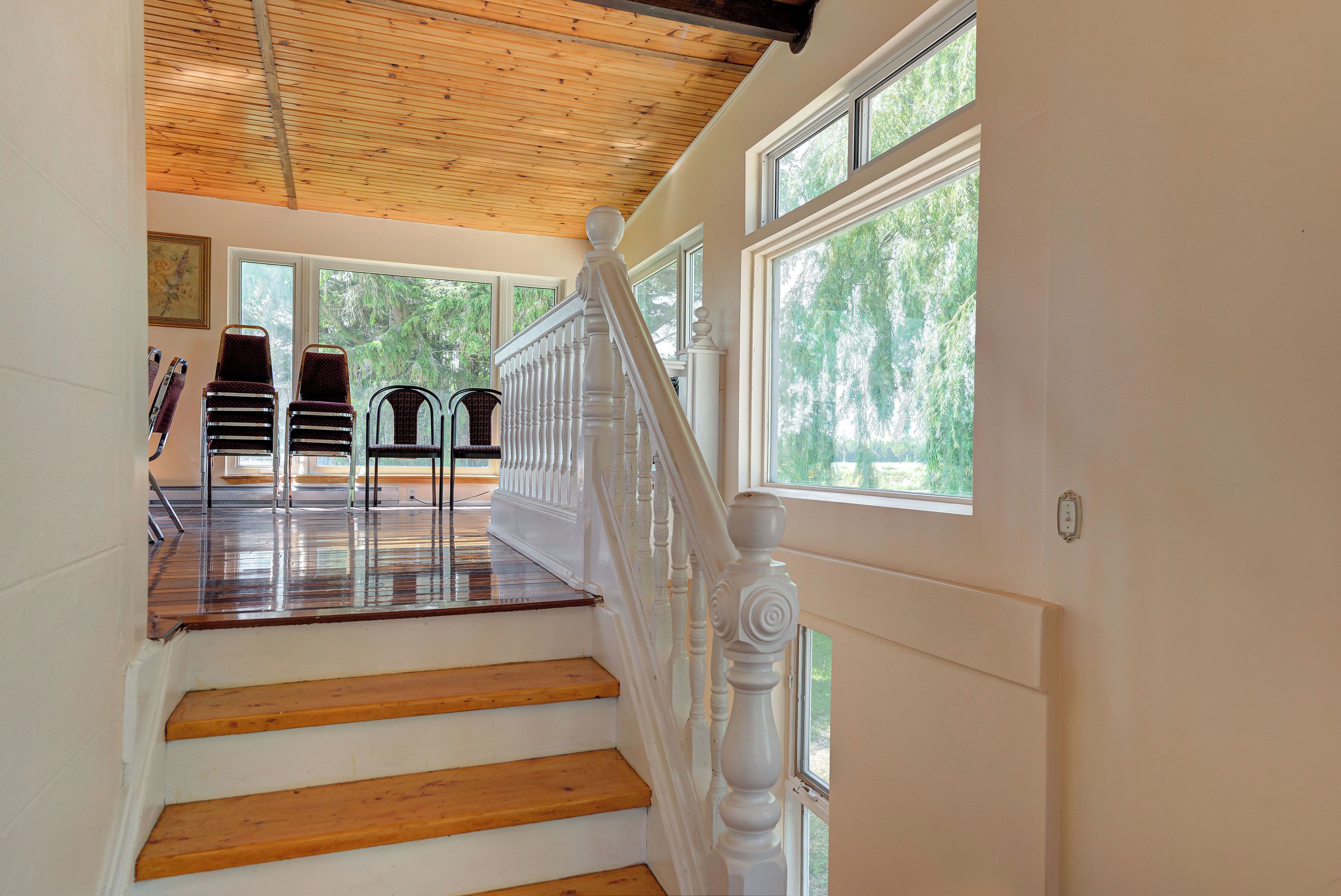 A wooden staircase with white railings leading to a room with large windows and a view of trees.