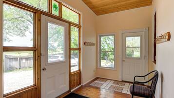 A hallway with wooden floors, a chair, and a door with a window.