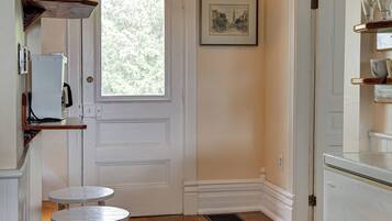 A kitchen with wooden flooring, a white door, a hanging light fixture, and a window.