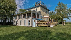 Une maison à deux étages avec un balcon, une véranda couverte avec une table et des chaises, et une cour gazonnée.