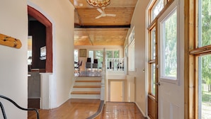 Un escalier en bois mène au deuxième étage, où l’on trouve une balustrade blanche, un ventilateur de plafond et de grandes fenêtres qui laissent entrer la lumière naturelle.