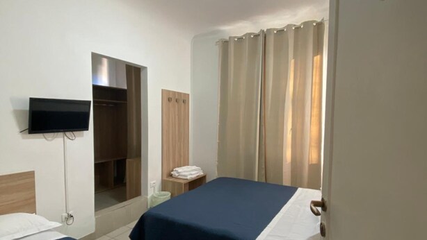 A hotel room with two beds, a TV mounted on the wall, a wardrobe, and a bathroom visible through an open door.