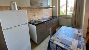 A compact kitchen with a refrigerator, a sink, and a window with curtains.