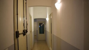 A narrow hallway with doors on both sides, a light fixture on the right wall, and a door at the end leading to another room.
