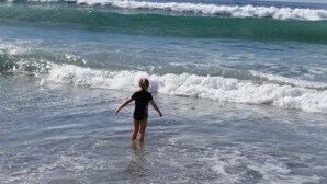 En person står i det flade vand ved stranden.