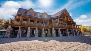 A large log cabin with multiple balconies and stone pillars, surrounded by a gravel driveway.