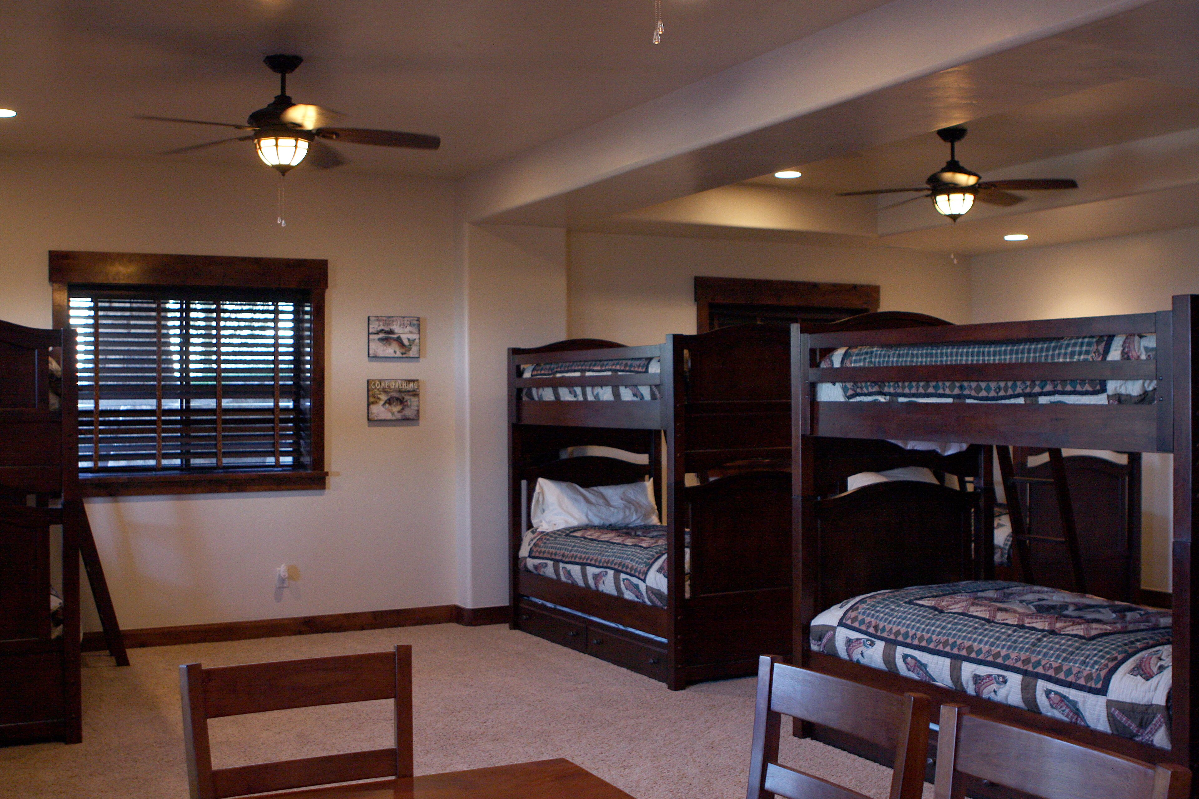 A room with two bunk beds, a wooden desk, a chair, and a ceiling fan.