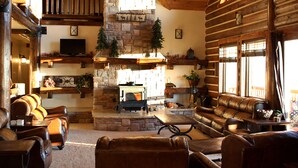 A log cabin interior with a stone fireplace, leather sofas, and a television.