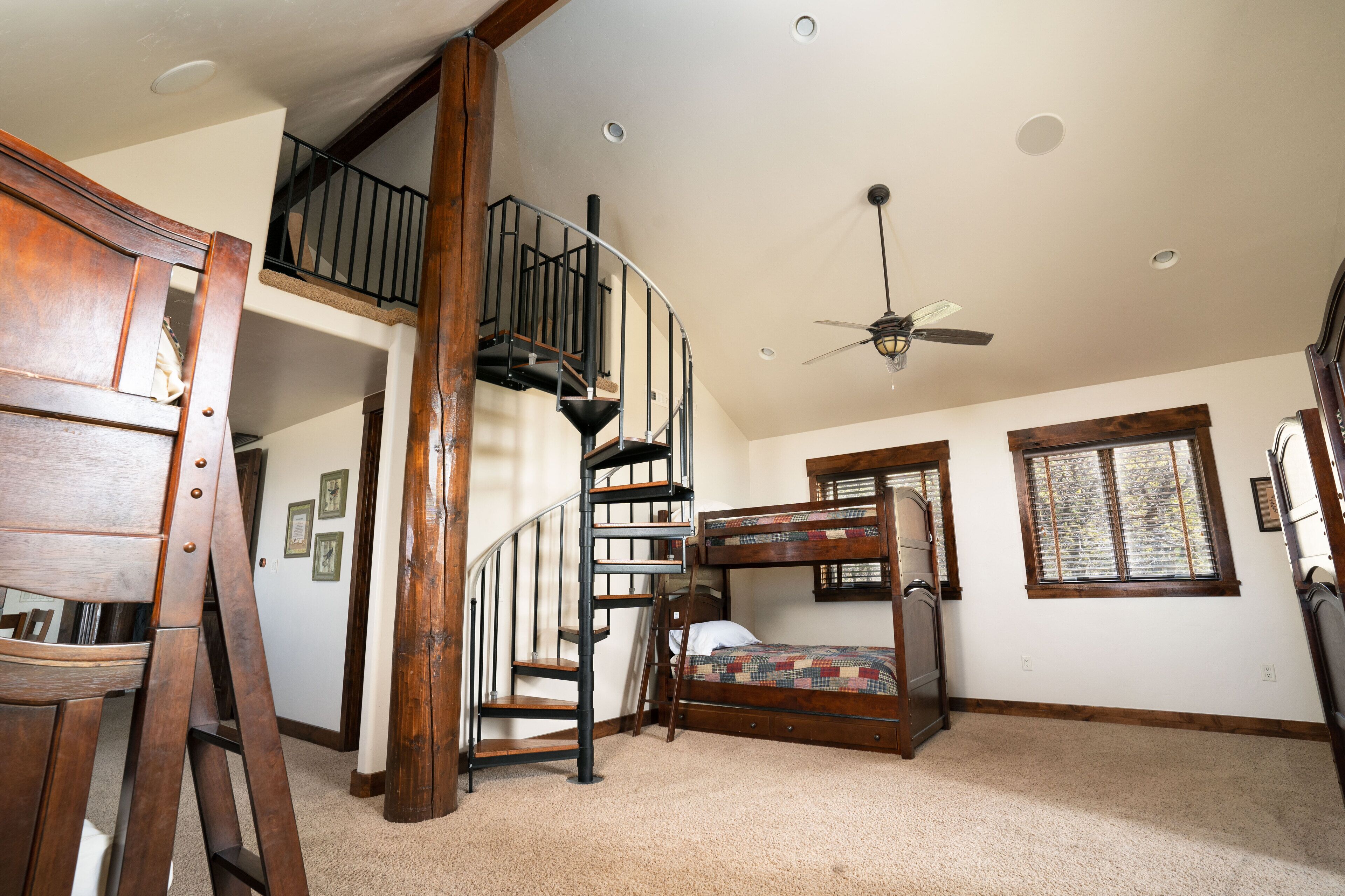 A bedroom with a bunk bed, a wooden staircase, a ceiling fan, and a window.