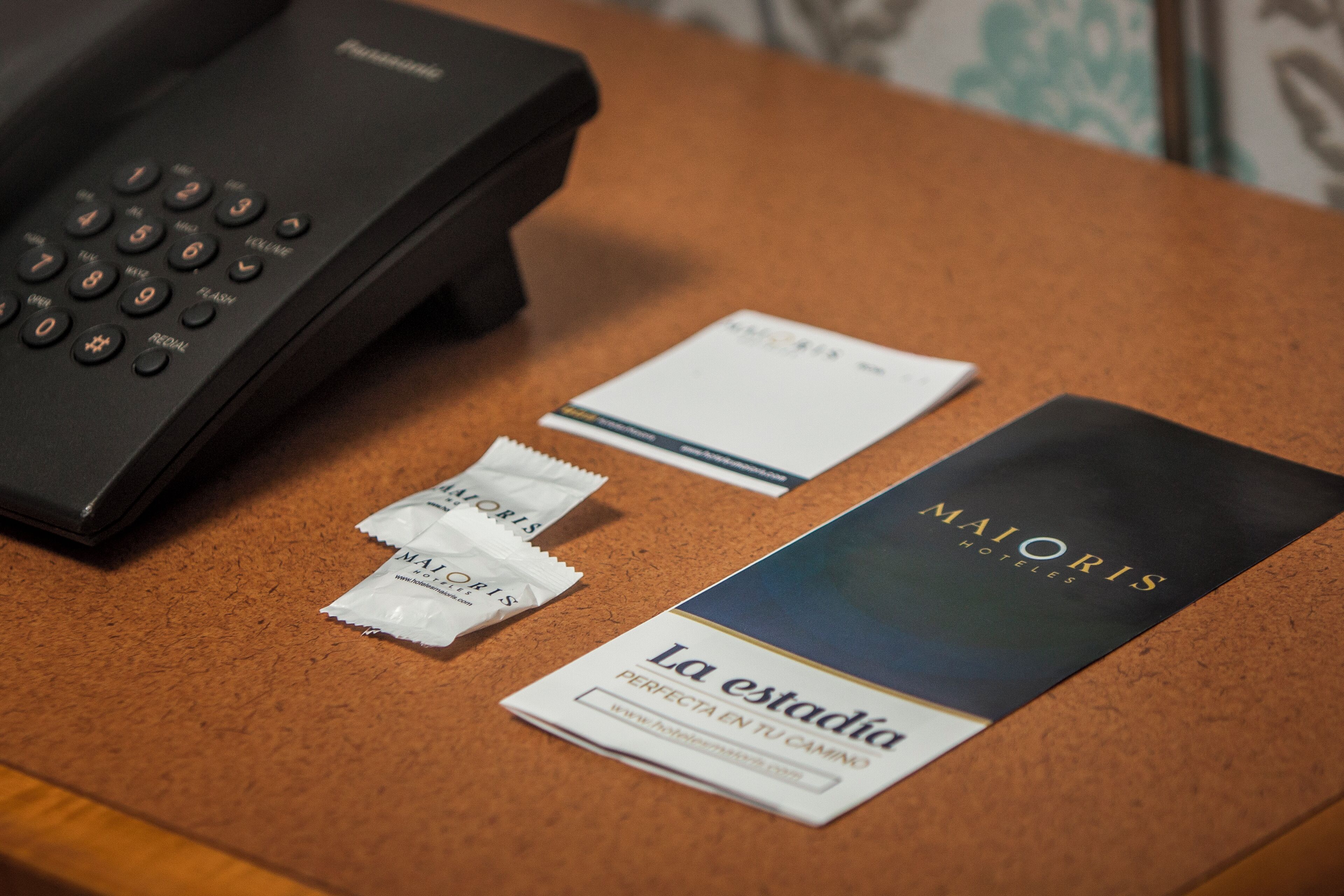 A hotel brochure, a telephone, and some packets on a corkboard.